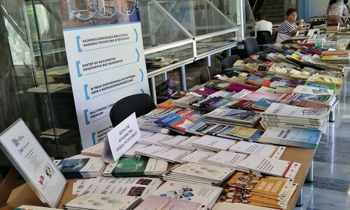 Długi st&oacute;ł z ofertą r&oacute;żnych wydawnictw , w tle baner biblioteki
